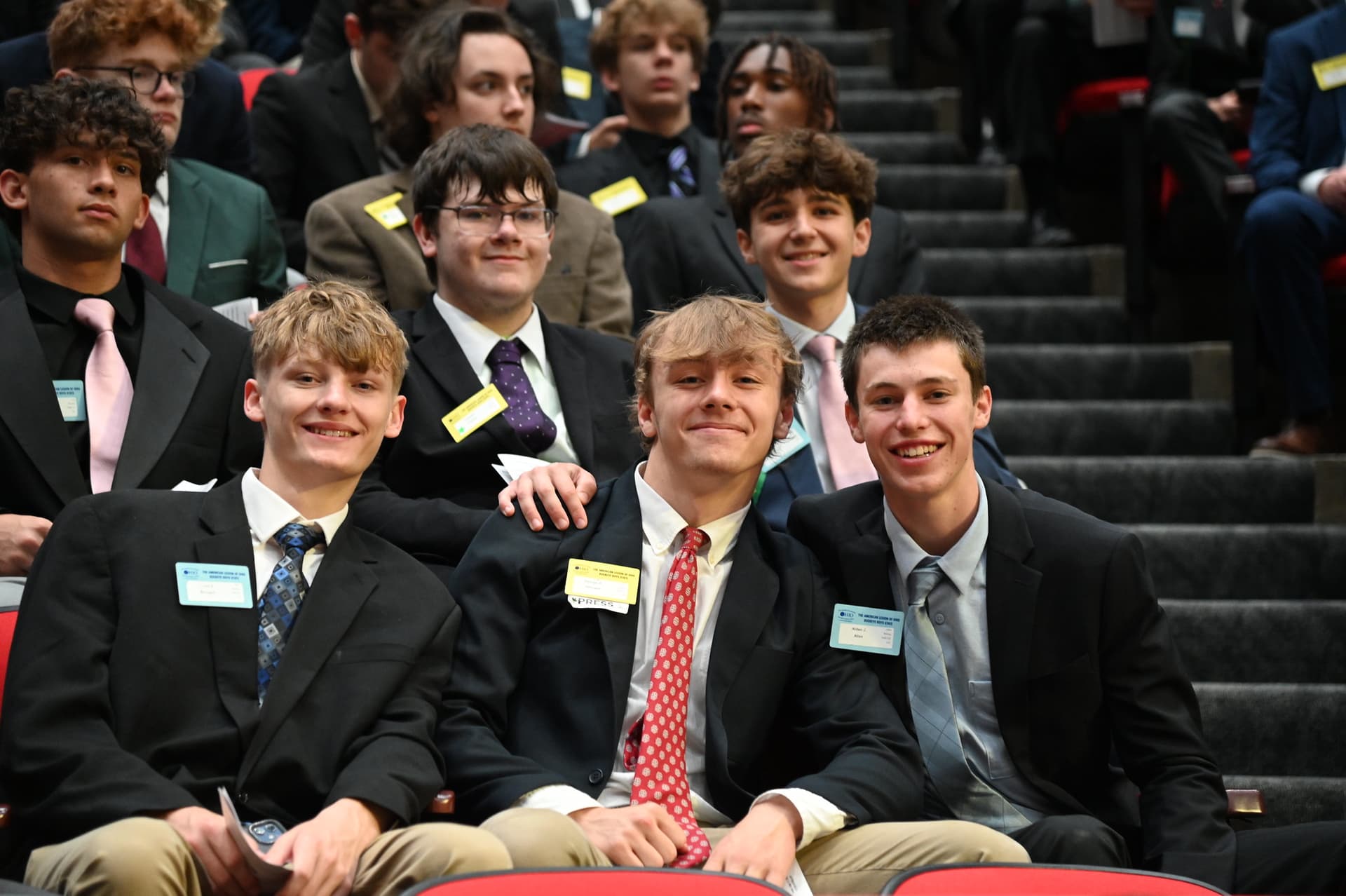 Three students in suits smiling at an evening assembly