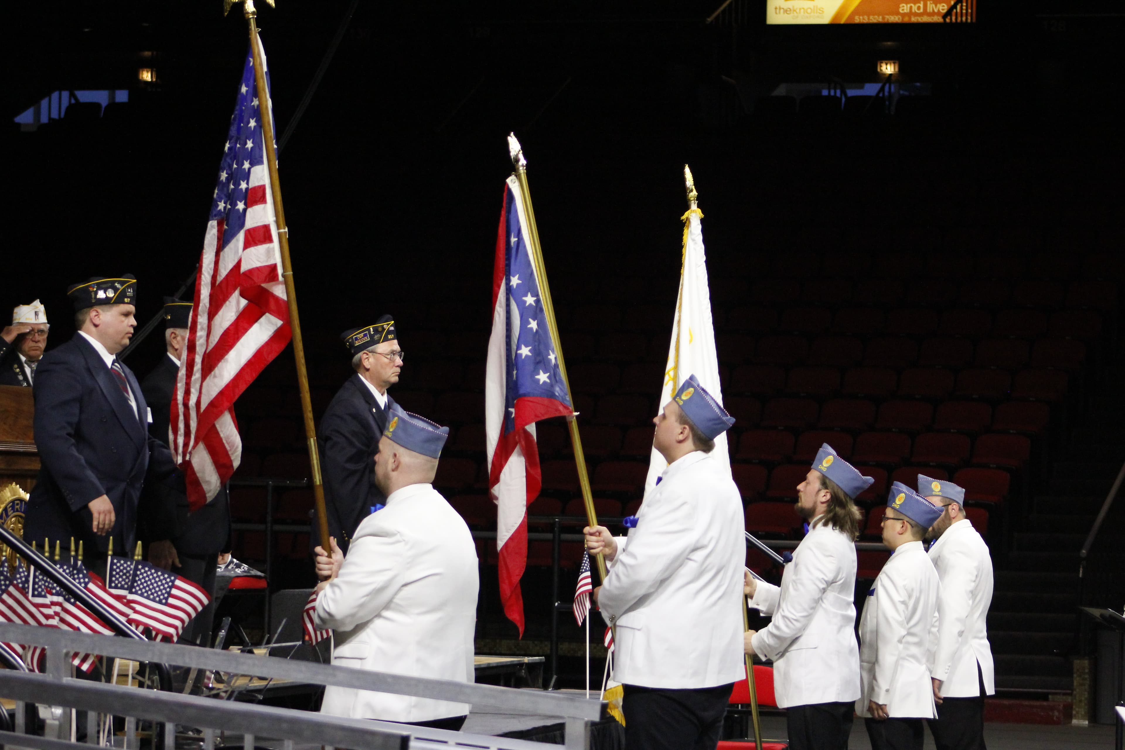 Five men in white suits presenting various flags at a stage