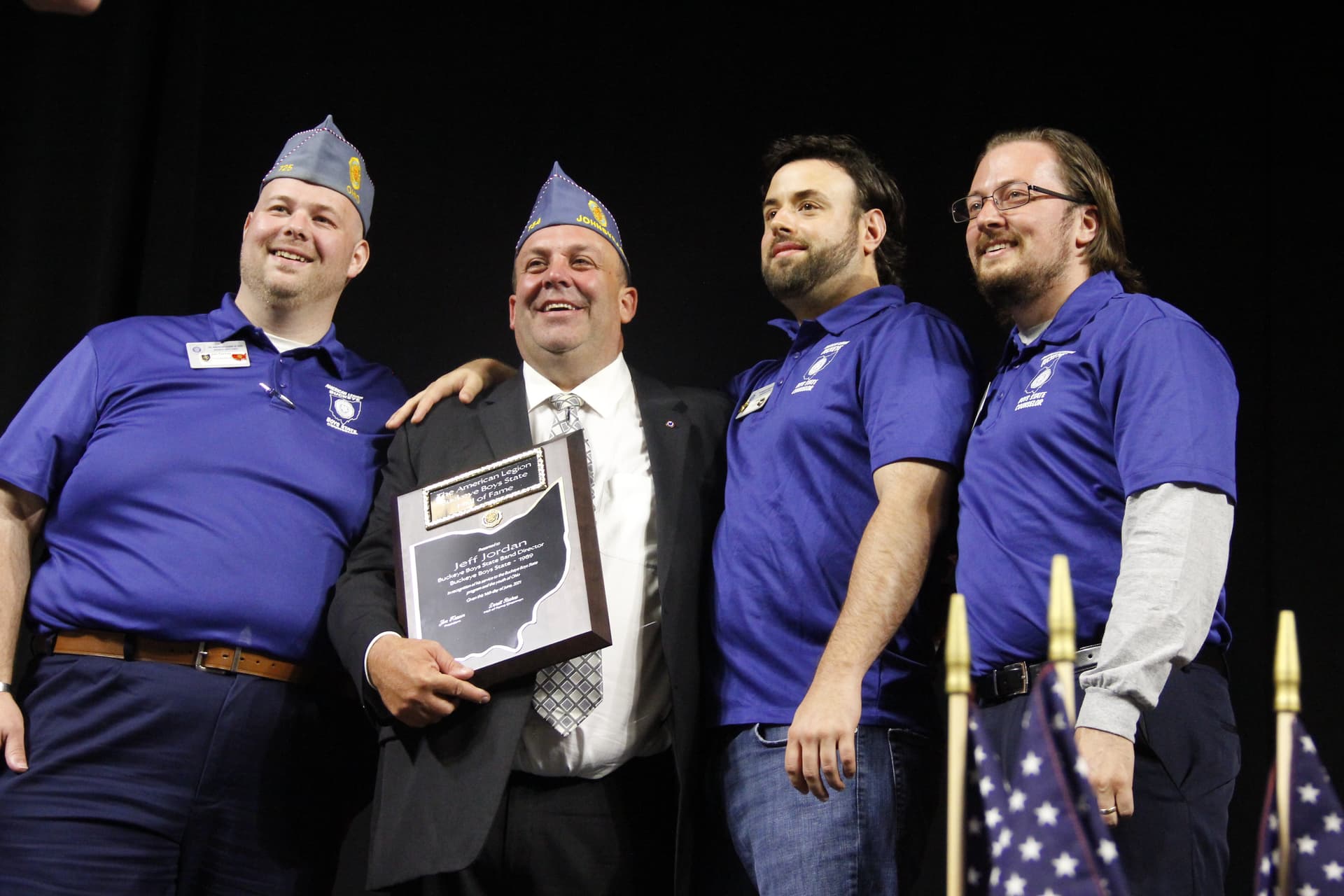 Three men on stage posing with a man holding an award plaque